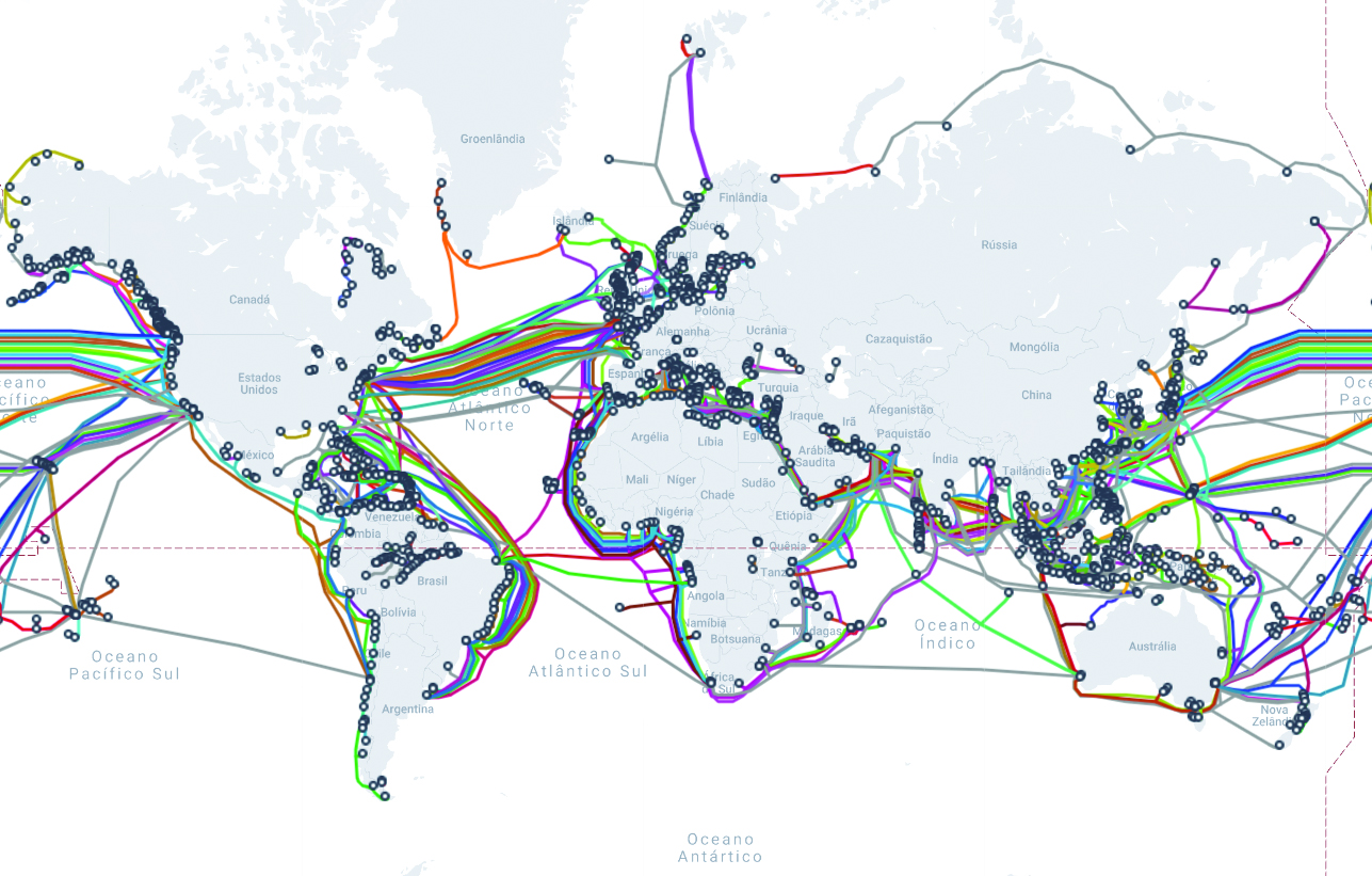 Planisfério com centenas de linhas coloridas representando os cabos submarinos de fibra óptica que cruzam os oceanos e conectam os continentes. Os traçados se concentram no Atlântico Norte, entre a América do Norte e a Europa; no Oceano Pacífico, junto às bordas do mapa, entre a Ásia e a América do Norte; e ao longo das costas da América do Sul, da África e do sul da Ásia. Pequenos círculos marcam os pontos onde os cabos chegam ao litoral, como no Nordeste brasileiro, na Europa e no leste da Ásia.